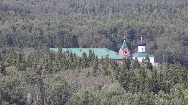View of the Solovetsky Monastery building with its distinctive green roof and dark dome nestled within a dense coniferous forest in Solovetsky, Arkhangelsk Oblast, Russia.