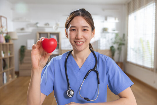 Healthcare and heart health concept. smiling nurse holding red heart symbol while wearing stethoscope in clinic. nurse, healthcare, heart, cardiology, wellness.