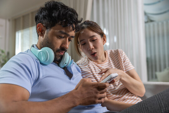 couple using smartphone together at home, sharing digital content and reacting to the screen, representing mobile technology, social media, communication, entertainment, connection.