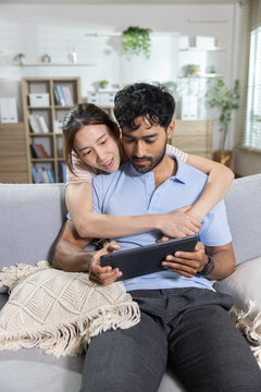 Happy couple concept. Smiling couple relaxes together on sofa while using tablet at home, enjoying digital entertainment. Couple, lifestyle, tablet, home, happiness.