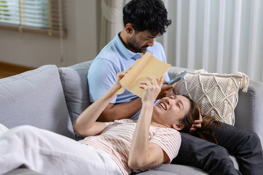 Relaxing couple concept. woman reads a book with her head on man lap as he uses smartphone on sofa at home. Couple, relaxing, lifestyle, reading, smartphone
