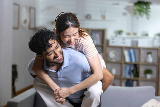 Happy young couple having fun at home as smiling woman enjoys piggyback ride with man, representing love, happiness, playful relationship, togetherness, affection joyful lifestyle.