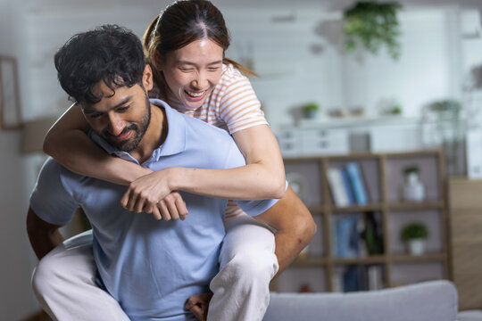Happy young couple having fun at home as smiling woman enjoys piggyback ride with man, representing love, happiness, playful relationship, togetherness, affection joyful lifestyle.