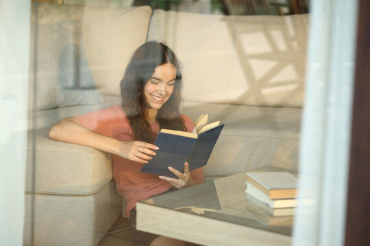 Happy teenager reading a paper book viewed through a window