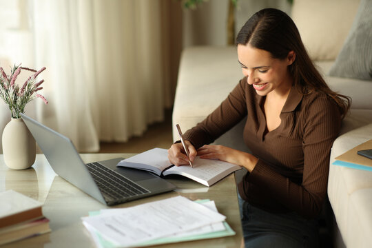 Happy woman telecommuting writing in agenda at home