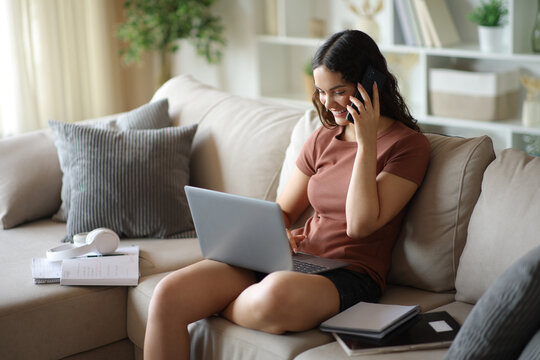 Happy student talking on phone and checking laptop at home
