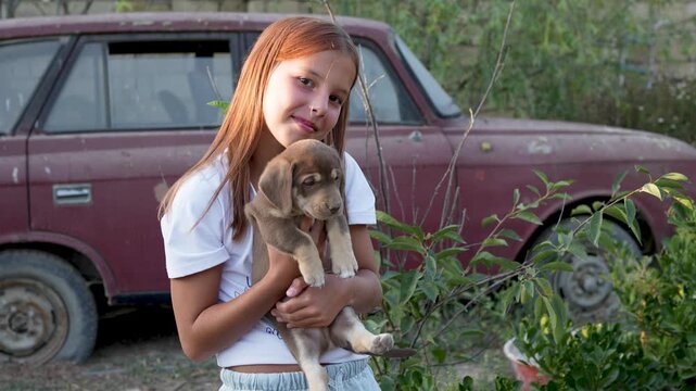 Happy girl holding cute puppy outdoors in country yard background