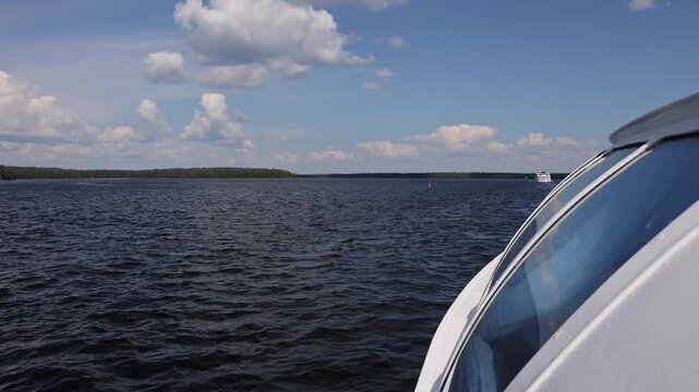 View of Lake Onega from a boat with calm water and distant forested shoreline under a blue sky in Petrozavodsk, Republic of Karelia, Russia.