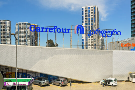 Batumi, Georgia - May 20, 2026: Large blue Carrefour supermarket logo sign on shopping mall building roof with city high rise skyscrapers behind under clear sky
