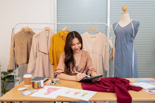 Young asian fashion designer drawing clothing design on digital tablet in tailoring studio