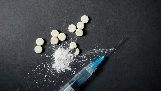Top view of some pills and syringe on black background. Misused concept of drugs. 