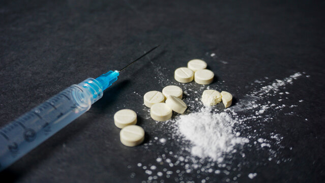 Misused concept of drugs, a syringe with some white drugs in powder and pill form. Close up angle. 