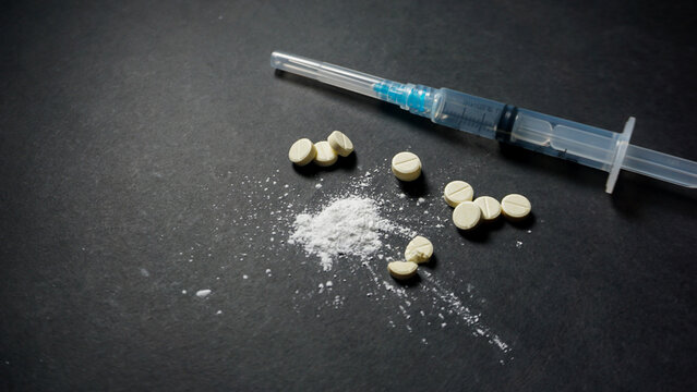 Some white illegal drugs in powder and pill form with one sealed disposable syringe. Misused concept of drug. 