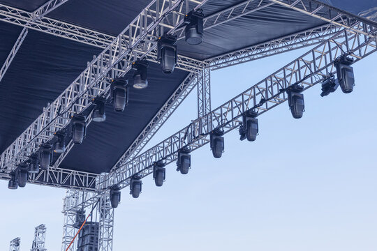 Metal stage truss structure supporting multiple professional moving head spotlights and sound equipment under a clear blue sky