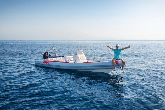 A happy captain sits on his RIB motorboat and enjoys the calm ocean on a summer day