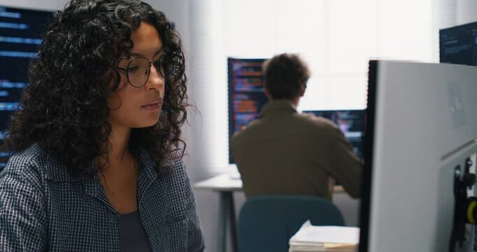 Latin woman leads a small team in the server room, coding detection rules while teammates monitor network traffic.