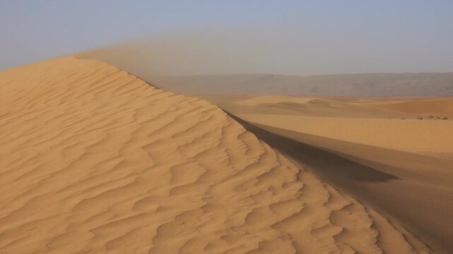 View of Sahara Desert sand dunes with wind blowing sand across the ripples in the vast landscape of Morocco.