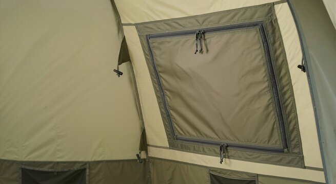 Closed ventilation window with zippers inside a camping tent. Interior detail of green and tan fabric outdoor shelter