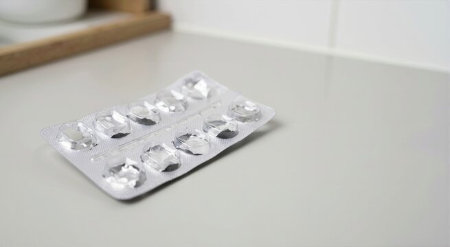 Empty silver foil blister pack on a grey counter. Used medication packaging with broken plastic holes. Finished prescription pills concept