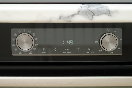 Modern oven control panel with digital timer and metal knobs under marble kitchen counter. New kitchen appliance with display for cooking temperature settings. Home technology concept.