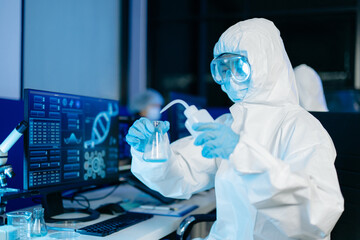 Scientist in protective hazmat suit analyzes DNA data and scientific charts on a modern computer...