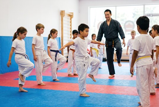 Kids are engaged in a martial arts class at a children's camp. They wear uniforms and focus on their movements while a teacher guides them