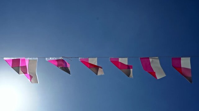 Red and white Indonesian national pennants hanging on a string line against a clear blue sky, celebrating independence day in bright sunlight.