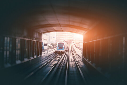 Modern train arriving at a station, light illuminating the end of a tunnel leading to an urban landscape