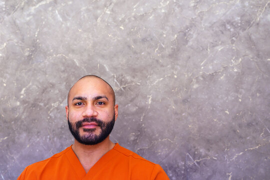 Male beautician in orange uniform working at a beauty salon reception desk, looking at camera