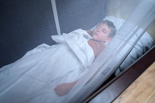 Child sleeping on a bed in a train carriage behind a protective safety net. Boy resting in a railway cabin bunk. Concept of safe comfortable travel during a long journey by railway.
