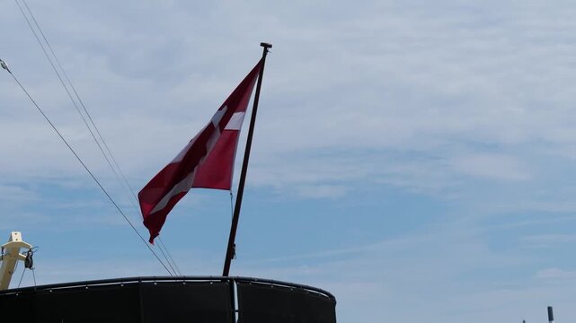 View of the red and white Danish flag waving in the wind on a ship against a cloudy sky in Copenhagen, Denmark.