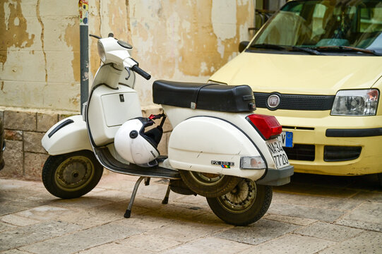 White Vespa PX 125 E scooter parked in front of a yellow Fiat Panda in an old town alley, classic vintage Italian scooter, Gallipoli, Puglia, Southern Italy 25.11.2025