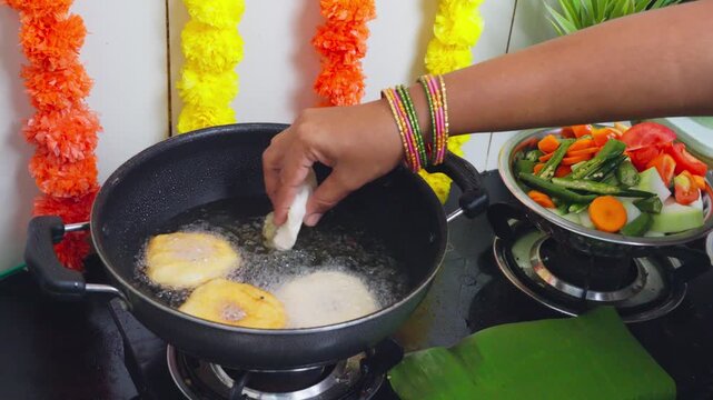 View of traditional Indian festival food frying in a pan with fresh vegetables and marigold garlands in the kitchen in Vijayawada, Andhra Pradesh, India.