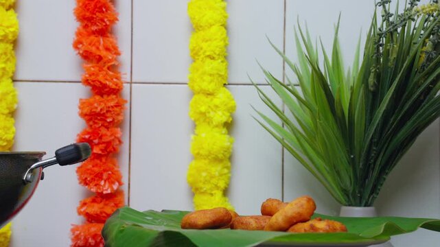 Golden medu vada dropping slow on a banana leaf for a festive feast with traditional diwali decorations in the background in Vijayawada, Andhra Pradesh, India.