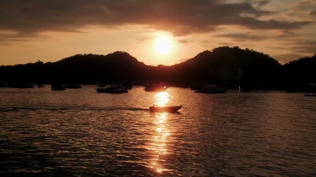 View of Labuan Bajo bay at sunset with small boats silhouetted against the golden sun reflecting on the calm water in Komodo, East Nusa Tenggara, Indonesia.