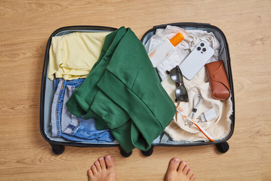 Top View of Open Travel Suitcase Packed with Clothes and Accessories on Wooden Floor