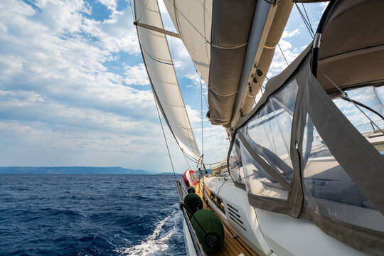 Dynamic view from deck of sailing yacht heeling under wind power while cutting through Adriatic waters. White wake, filled sails, a sense of speed, freedom and offshore adventure