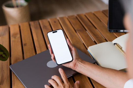 White Person holding smartphone with blank screen over wooden desk
