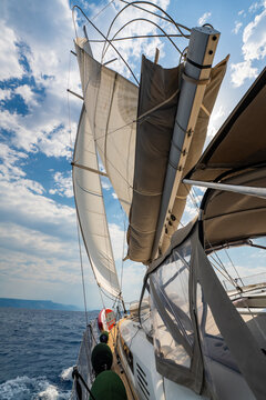 Low angle view of sailing yacht with fully deployed sails, taut rigging and windblown lines while cruising across Adriatic Sea. Dynamic maritime scene highlighting wind power, seamanship and freedom.