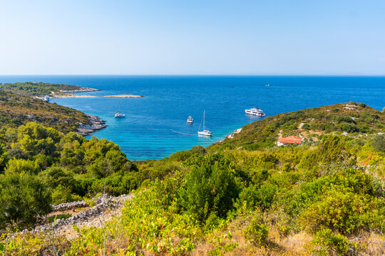 Scenic coastal bay with anchored yachts, turquoise Adriatic Sea, rocky shoreline and lush Mediterranean vegetation on Vis Island in Croatia. Ideal destination for sailing, boating and summer vacation