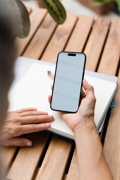 White Person holding smartphone over notebook on wooden table