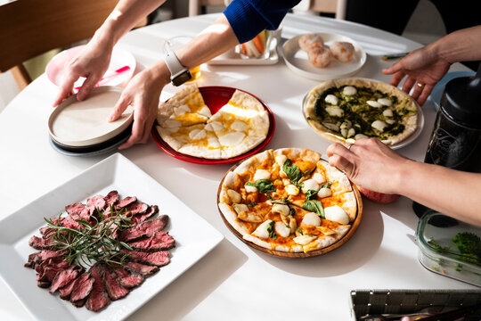 Hands Setting Up Home Party Dining Table with Roast Beef and Pizzas