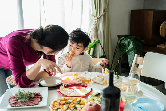 Asian Mother Leaning Over Talking to Son Eating Pizza Slice at Dining Table