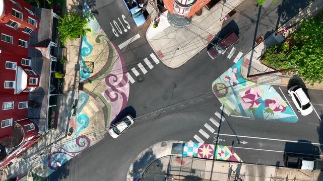 Aerial view of colorful street murals at city intersection with moving cars in bright daylight.