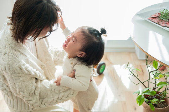 Crying Asian Toddler Girl Standing Held by Mother Comforting Her at Home