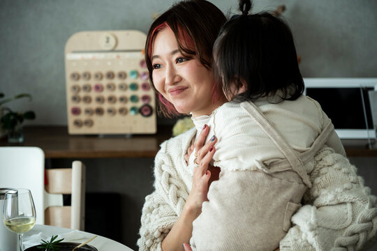 Asian Mother Holding Toddler Daughter Softly Looking at Her Indoors at Home