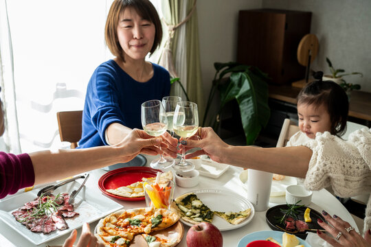 Smiling Asian Friends Toasting with Wine Glasses around Home Party Dining Table