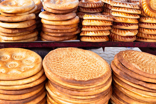 Stacks of traditional Uzbek flatbread displayed at a bazaar in Bukhara. Golden round loaves with decorative stamped patterns fill the frame, ideal for food culture and travel content.