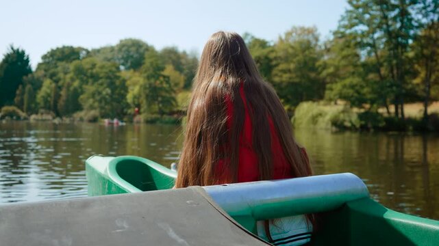Teenage girl canoeing across calm park lake during sunny summer day. Young paddler enjoying peaceful water activity. Youth adventure, outdoor recreation and healthy lifestyle