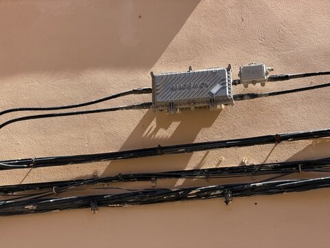 Manacor, spain, august 30, 2026, magnavox cable tv amplifier box and multiple black telecommunication wires installed on an outdoor building wall